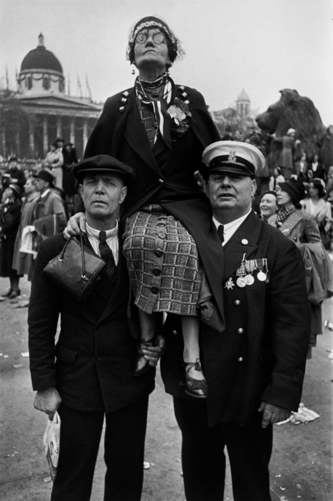 Eine neugierige Frau sitzt auf den Schultern von zwei Männern, um die Krönung von Geirge VI in London besser sehen zu können. Foto aus der Ausstellung zu Henri Cartier-Bresson im Foto Arsenal Wien 2025